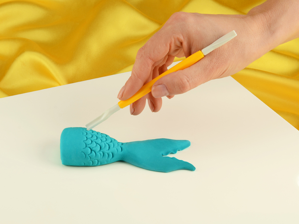 Modellieranleitung Meerjungfrauenflosse - Schwanzflosse wird mit den Fingern ausgeduennt und Schuppenmuster mit einem Modellierwerkzeug gepraegt