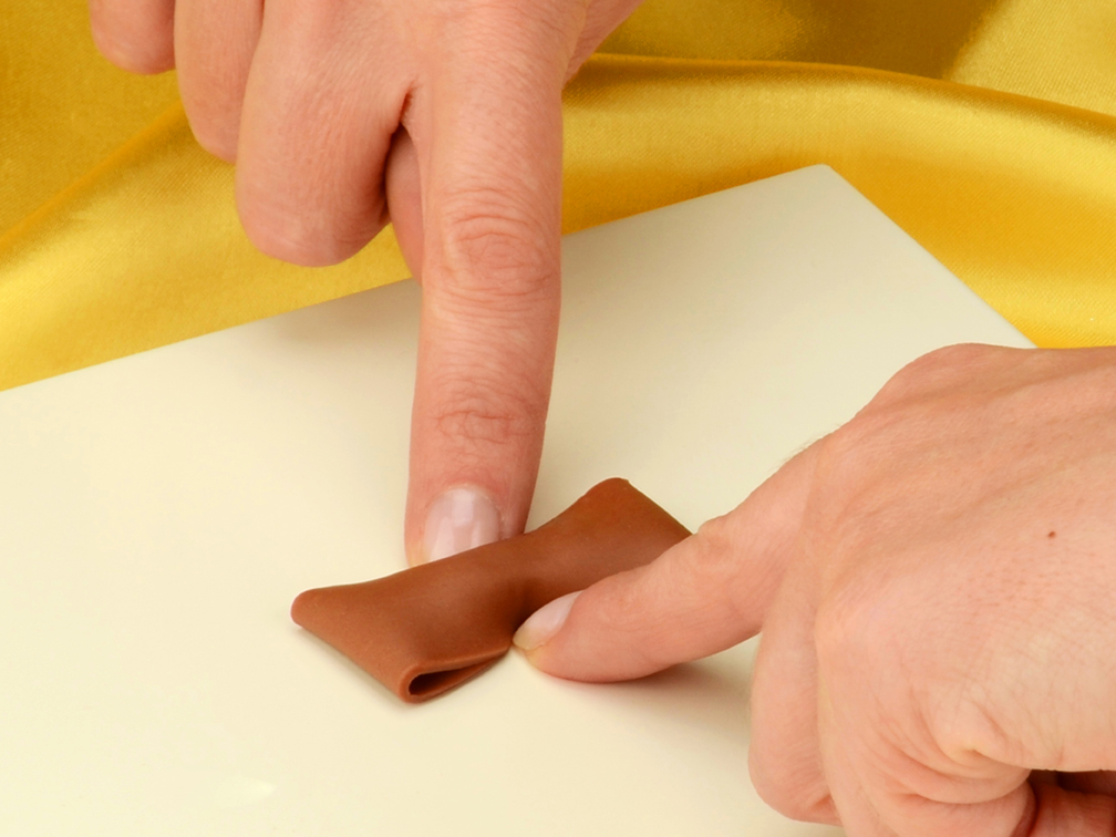 Modellieranleitung Schleife - Modellierschokolade wird umgedreht und die Mitte mit zwei Fingern zusammengedrueckt