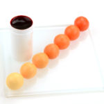 Foto zeigt einen Behaelter gefuellt mit Pastenfarbe apricot und Fondantkugeln mit den moeglichen Farbabstufungen